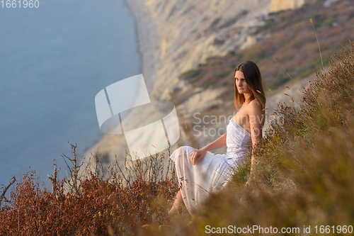 Image of A beautiful girl in a white dress enjoys a beautiful view from the mountain to the sea at sunset