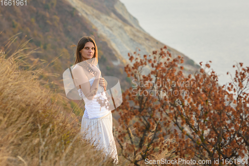 Image of Beautiful girl in white dress hugging wild flowers on the background of beautiful scenery