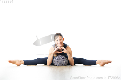 Image of Restorative yoga with a bolster. Young sporty female yoga instructor in bright white yoga studio, lying on bolster cushion, stretching, smilling, showing love and passion for restorative yoga