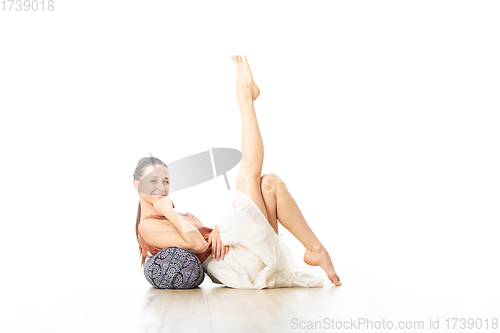 Image of Restorative yoga with a bolster. Young sporty female yoga instructor in bright white yoga studio, lying on bolster cushion, stretching, smilling, showing love and passion for restorative yoga