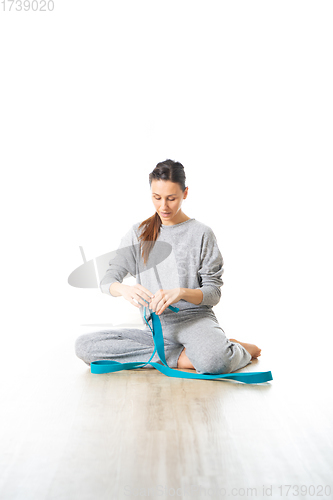 Image of Young sporty female yoga instructor in bright white yoga studio, smiling cheerfully while preparing yoga exercise props