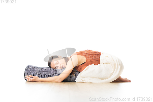 Image of Restorative yoga with a bolster. Young sporty attractive woman in bright white yoga studio, lying on bolster cushion, stretching and relaxing during restorative yoga. Healthy active lifestyle