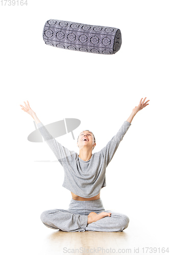 Image of Restorative yoga with a bolster. Young sporty female yoga instructor in bright white yoga studio, throwing bolster cushion in air , smilling, showing love and passion for restorative yoga