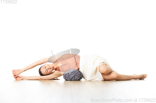 Image of Restorative yoga with a bolster. Young sporty attractive woman in bright white yoga studio, lying on bolster cushion, stretching and relaxing during restorative yoga. Healthy active lifestyle