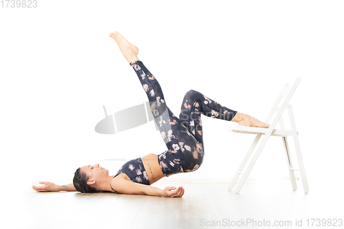 Image of Young sporty attractive woman in bright white yoga studio, stretching and relaxing during restorative yoga using white chair as a gadget. Healthy active lifestyle