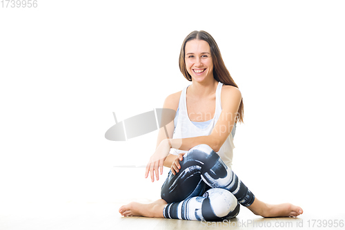 Image of Young sporty female yoga instructor in bright white yoga studio, smiling cheerfully, looking at the camera.