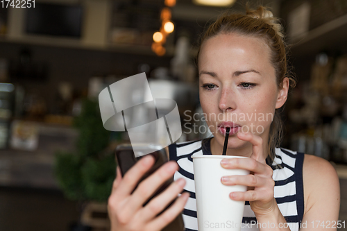 Image of Thoughtful woman reading news on mobile phone while sipping coffee in coffee shop.