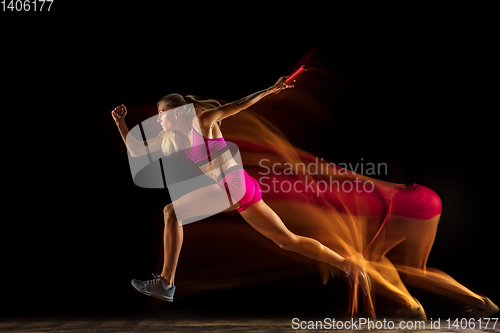 Image of Professional female relay racer training on black studio background in mixed light