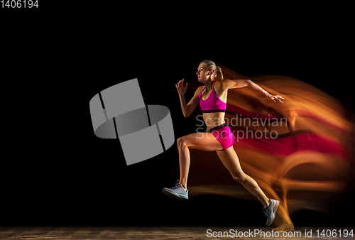 Image of Professional female relay racer training on black studio background in mixed light