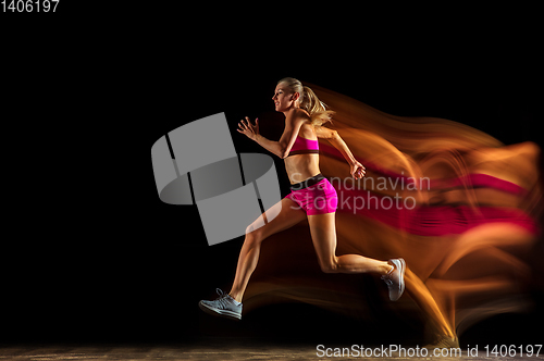 Image of Professional female relay racer training on black studio background in mixed light