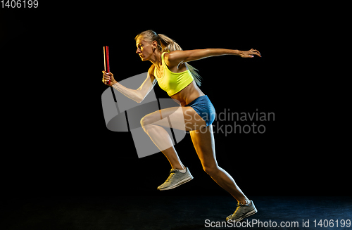 Image of Professional female relay racer training on black studio background in neon light