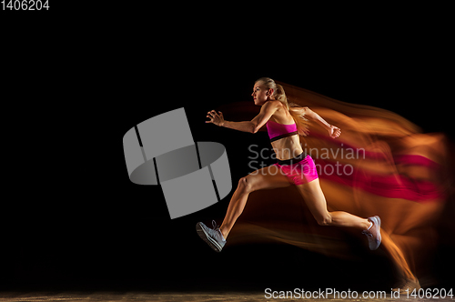 Image of Professional female relay racer training on black studio background in mixed light