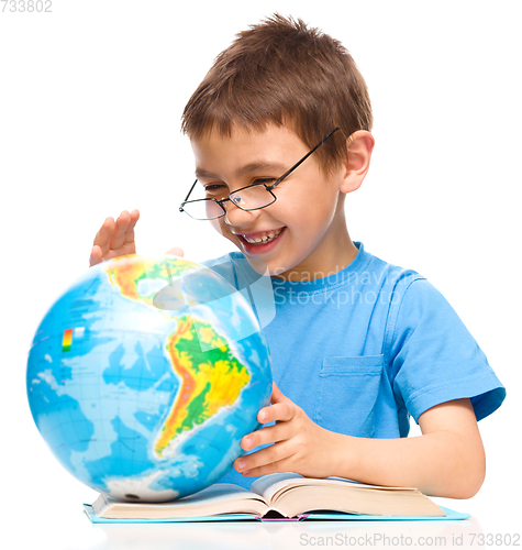 Image of Little boy is examining globe