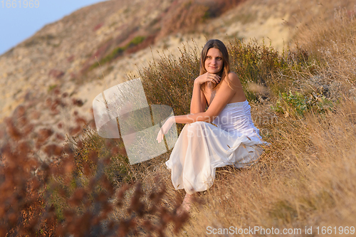 Image of Beautiful girl sitting on a hillside at sunset