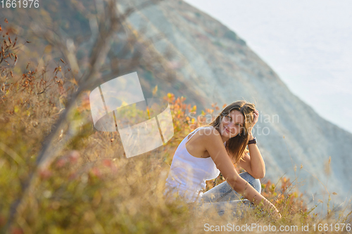 Image of Happy girl sitting on the mountainside and happily looking at the landscape