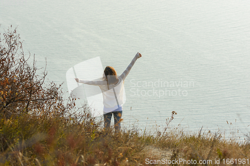 Image of Happy girl happily raised her hands up enjoying the seascape, view from the back