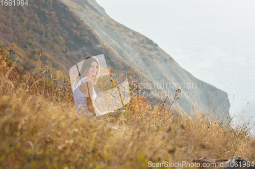 Image of The girl is sitting on the mountainside and turning around looked into the frame