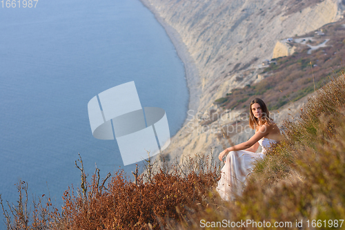 Image of Beautiful girl at sunset sitting on a rocky beach