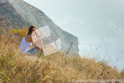 Image of The girl sat down on the mountainside and looks at the seascape