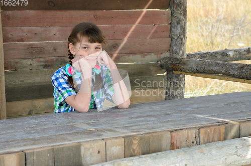 Image of Portrait of a beautiful girl of ten years old sitting at a wooden table in nature