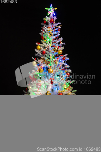 Image of Festively decorated artificial white Christmas tree on a black background