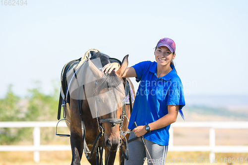 Image of Portrait of a beautiful girl in casual clothes standing next to a horse and joyfully looking into the frame