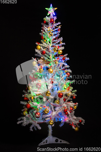 Image of Festively decorated artificial white Christmas tree on a black background