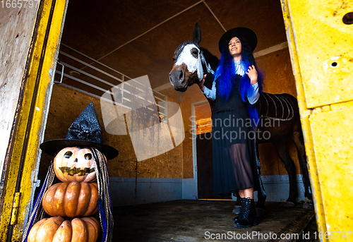 Image of A girl dressed as a witch comes out of the corral with a horse, in the foreground an evil figure of pumpkins