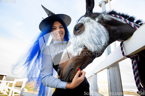 Image of A girl dressed as a witch stands next to a horse on which a skeleton is drawn for the celebration of Halloween