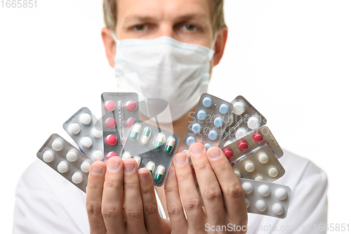 Image of A man in a medical mask holds a fan of medicines in front of him, focusing on medicines