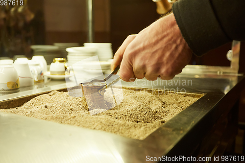 Image of Close up hands of a man cooking turkish coffee on hot golden sand.