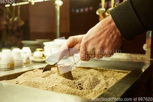 Image of Close up hands of a man cooking turkish coffee on hot golden sand.