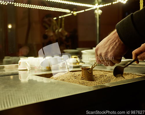 Image of Close up hands of a man cooking turkish coffee on hot golden sand.