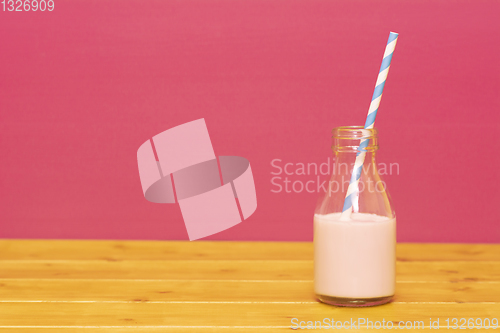 Image of Milk bottle half full with strawberry milkshake with a straw