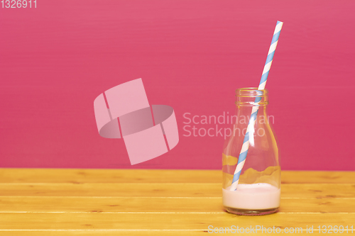 Image of Milk bottle with dregs of strawberry milkshake and a straw