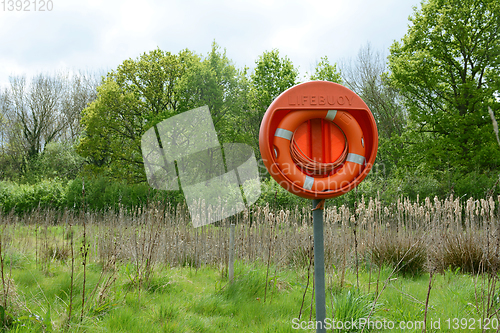 Image of Bright orange life belt on a pole near a deep pond filled with b