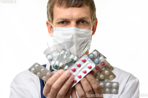 Image of A man in a medical mask holds a fan of medicines in front of him