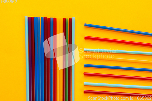 Image of On a yellow background, multicolored cocktail tubes lie, next to a bunch of vertical tubes lie horizontal