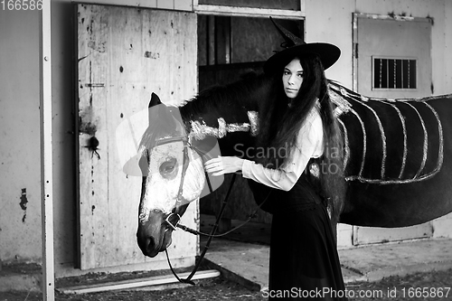 Image of Black and white portrait of a girl in a witch costume with a horse on which a skeleton is drawn