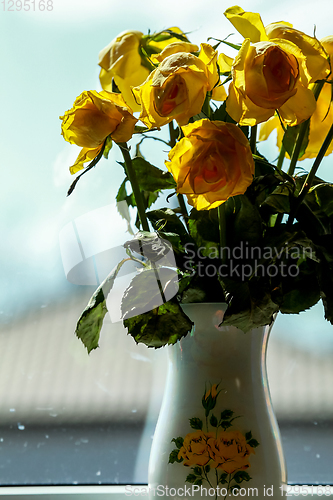 Image of Yellow roses in vase at the window.