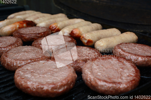 Image of Burgers and sausages starting to cook on a grill