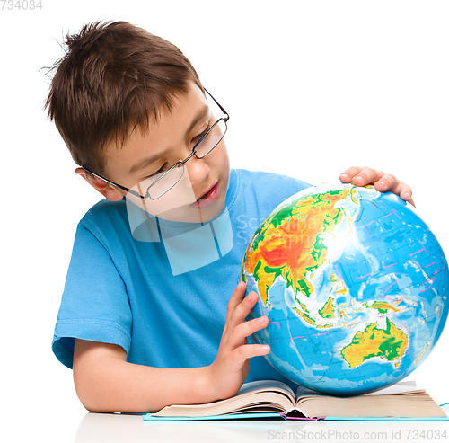 Image of Little boy is examining globe