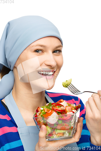 Image of Young attractive woman is eating salad using fork