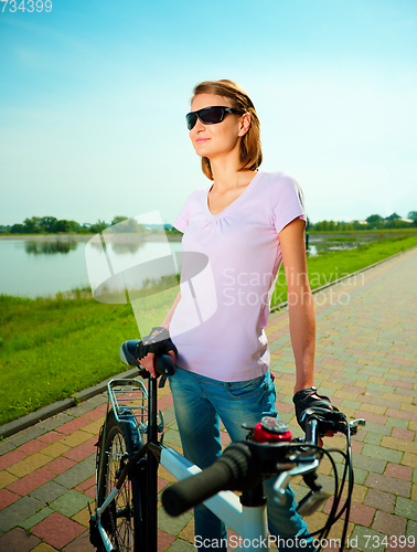 Image of Young woman is standing behind bicycle