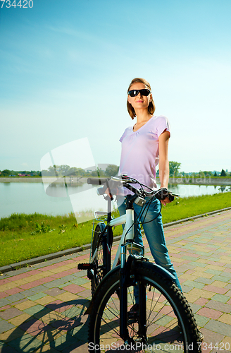 Image of Young woman is standing behind bicycle