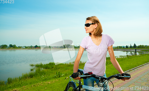 Image of Young woman is standing behind bicycle