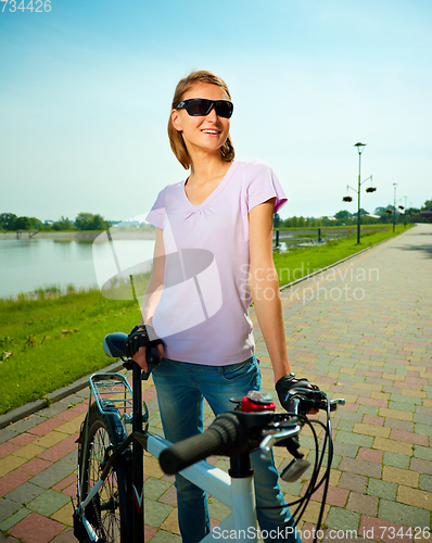 Image of Young woman is standing behind bicycle