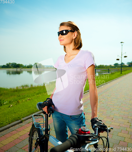 Image of Young woman is standing behind bicycle