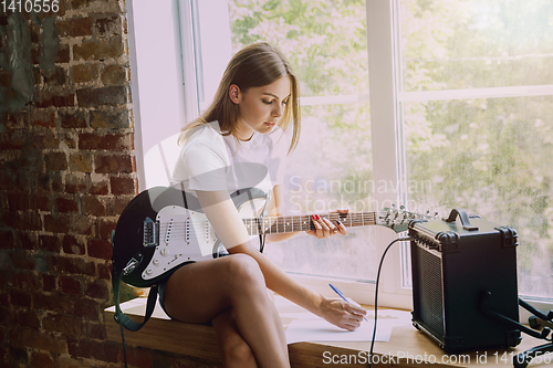 Image of Woman recording music, playing guitar and singing at home