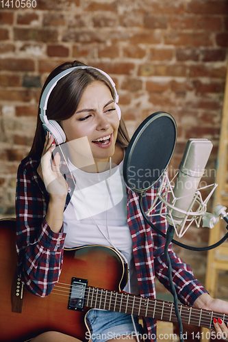 Image of Woman recording music, playing guitar and singing at home